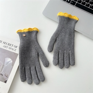 Détail de gants en tricot gris avec volants jaunes et bouton en métal sur un bureau blanc