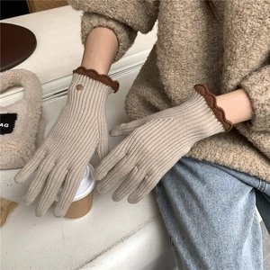 Détail de gants en tricot avec bords festonnés marron et bouton décoratif en métal doré