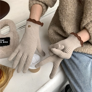Détail de gants en tricot beige avec bordure ondulée marron et bouton doré décoratif