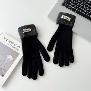 Flat lay of black knit gloves with grey cuffs on a desk with a laptop and a book