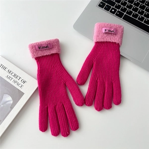 Close-up of pink knitted gloves with fuzzy sheepskin cuffs and brand label on desk