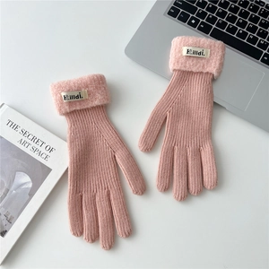 Detail of pink knitted gloves with white faux fur cuffs and brand label on a desk