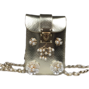 Macro detail of faux pearl clusters and resin flowers on a golden metallic phone bag