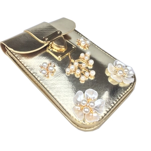 Detail of lychee pattern gold crossbody bag with pearl flowers and metal snap closure