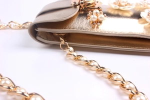 Detail of gold metal bag featuring white pearl flowers and pearl-woven chain strap