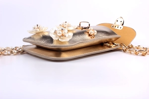 Detail of gold metallic crossbody bag featuring 3D pearl flowers and chain strap