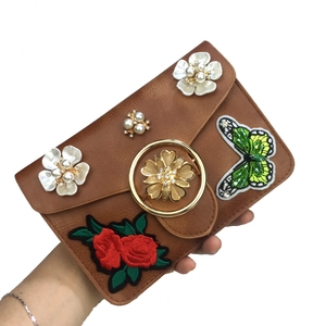 Détail du sac en cuir marron avec papillon brodé et décorations de fleurs en perles