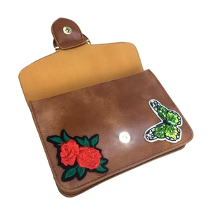 Détail de broderie roses rouges et papillon à paillettes vert sur sac en cuir marron