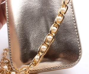 Macro detail of gold textured leather handbag with pearl-inlaid luxury metal chain