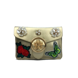 Détails du sac doré en cuir avec papillon en paillettes et fleurs de perles