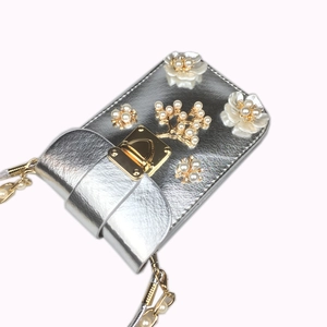 Detail of silver phone bag featuring pearl flower embroidery and a gold clasp