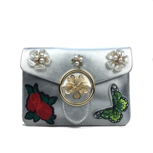 Détail de sac bandoulière argenté avec broderie de perles et papillon en strass brillant