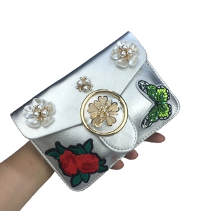 Détail de pochette en cuir argenté avec paillettes papillon et broderie de fleurs perlées