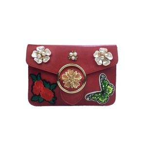 Détail d'un sac bandoulière rouge avec broderie de roses et fleurs de perles décoratives