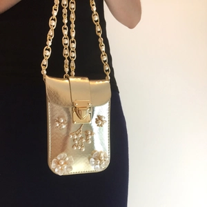 Detail of gold metal phone bag with pearl floral embroidery and chain strap on person