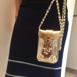 Detail view of a gold cross-body phone bag with pearl floral accents and chain strap
