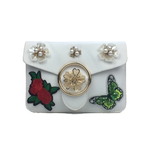 Détail du sac blanc avec fleurs en perles, broderie de rose et écusson papillon