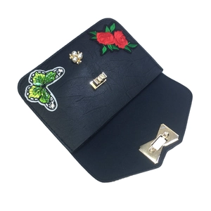 Detail of black faux leather envelope bag featuring butterfly embroidery and pearl buckle