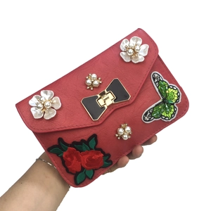 Detailed close-up of red pebbled leather bag with butterfly buckle and floral embroidery