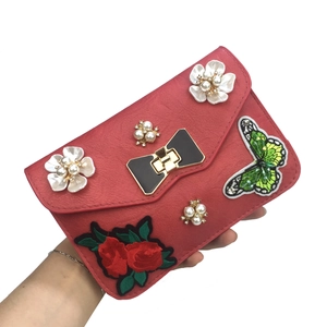 Close-up of red crossbody bag featuring 3D pearl flowers and green butterfly embroidery