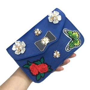 Detail of blue faux leather purse with butterfly embroidery and pearl flower accents