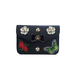 Detail of black crossbody bag with pearl flowers, rose embroidery and green butterfly