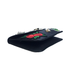 Detail of black crossbody bag featuring red rose embroidery and white pearl accents