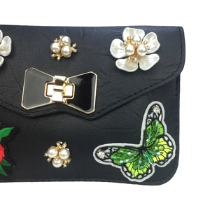 Black leather crossbody bag with butterfly embroidery, pearls, and a large bow buckle