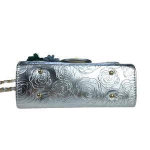 Detail view of silver rose-embossed bag base with four golden metal protective feet