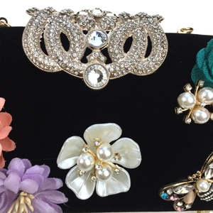 Detailed macro view of 3D flowers, pearls and jeweled butterfly on black velvet bag