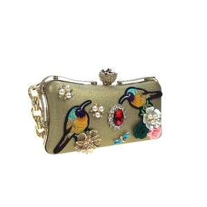Close-up of golden embroidery evening clutch with hummingbird and jewel details