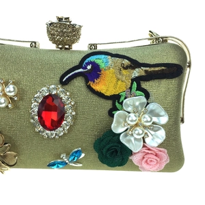 Detail of evening clutch with bird embroidery, red gemstone, and pearl flower accents