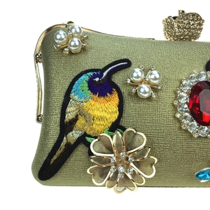Golden evening clutch bag with hummingbird embroidery, pearls, and a large red gemstone