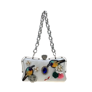 Macro view of bird embroidery and large blue gemstone on white leather evening clutch