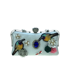 Close-up of bird embroidery, pearls and blue gemstone on ivory leather evening clutch