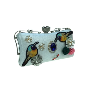 Close-up of bird embroidery and blue gemstone on a pearl-textured evening clutch bag