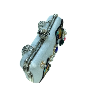 Detail of evening clutch featuring bird embroidery, pearls, and blue gemstones on silver fabric