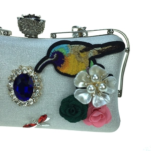 Detail of silver evening clutch with hummingbird embroidery and blue gemstone buckle