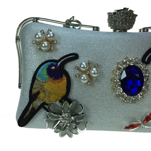 Detailed embroidery of hummingbird and blue gemstone on silver evening clutch bag
