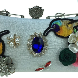 Macro detail of luxury evening bag with bird embroidery, floral motifs and a blue gemstone