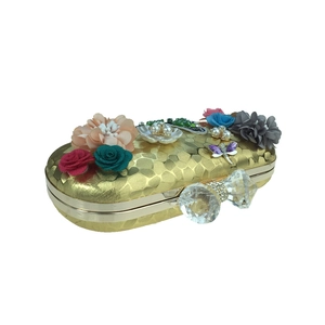 Détail d'une pochette de soirée dorée avec fleurs 3D et fermoir nœud en cristal