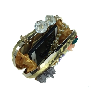 Pochette dorée avec fleurs en satin, cristaux et bandoulière chaîne sur fond blanc