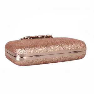 Macro detail of sparkly rose gold glitter clutch with a crystal-encrusted bow clasp