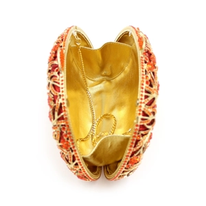 Detail of open gold hollow evening bag with red crystals and metallic chain strap