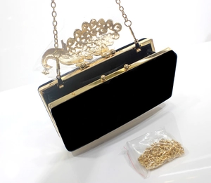 Detail einer schwarzen Samt-Abendtasche mit goldenem Pfauenverschluss und feiner Kette
