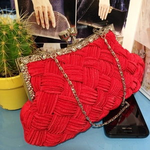 Macro shot of red woven satin clutch featuring rhinestone trim and a gold chain strap