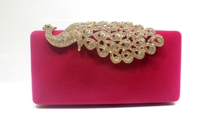 Detail einer fuchsiafarbenen Samt-Abendtasche mit goldener, kristallbesetzter Pfauenverzierung