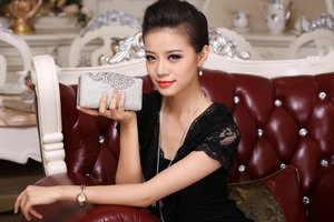 Silver clutch bag encrusted with white rhinestones held by a model on a leather sofa