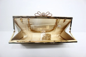 Detail of a gold evening clutch showing the satin lining, crystal bow clasp, and chain strap