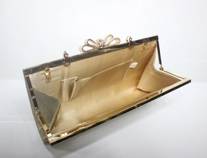 Detail view of champagne gold evening bag with rhinestone bow and satin interior lining
